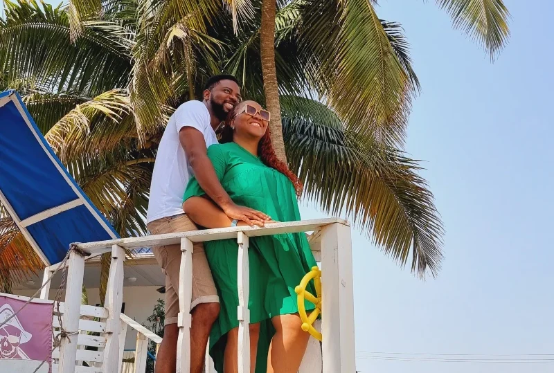 A couple enjoying a romantic moment at a tropical beachside destination in Nigeria, surrounded by palm trees.