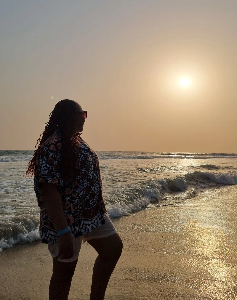 A woman standing at the shoreline during a beautiful sunset on a Nigerian beach, perfect for a romantic honeymoon.