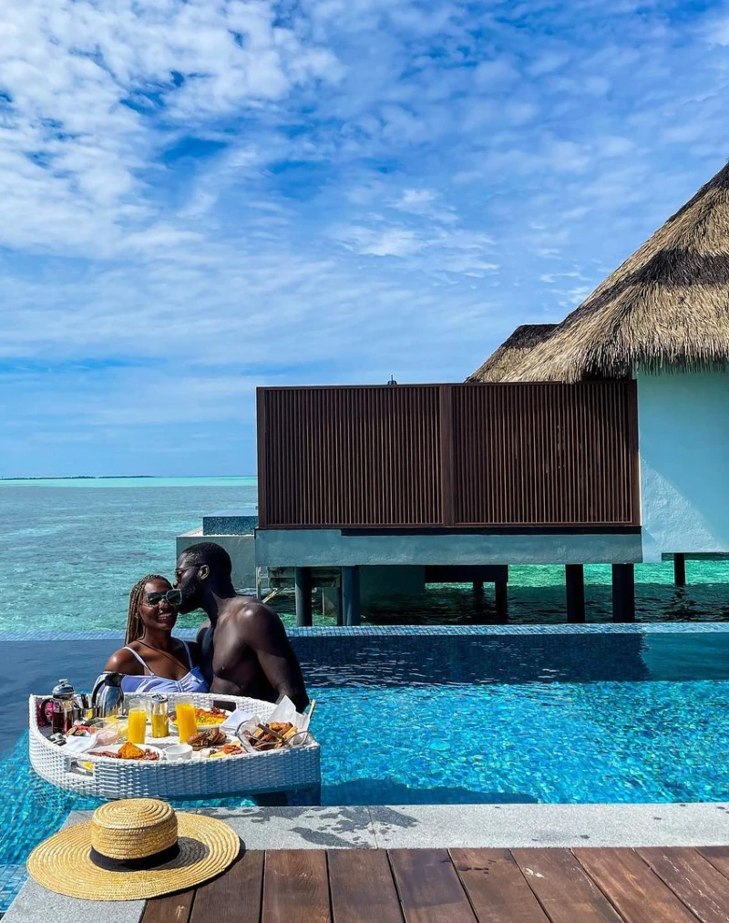 A couple enjoying a romantic floating breakfast in a luxury pool villa, set against a stunning backdrop of turquoise waters and overwater bungalows.