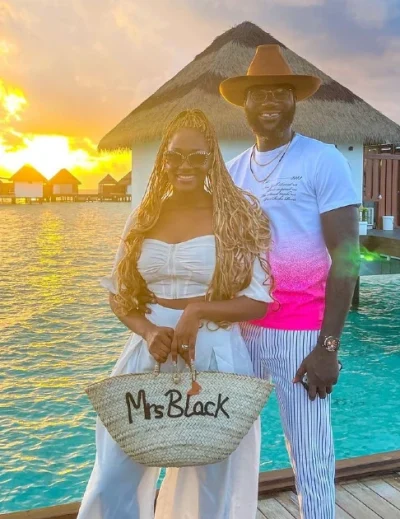 A smiling couple posing at sunset by the turquoise waters of a luxurious overwater bungalow, holding a customized bag that says 'Mrs. Black.