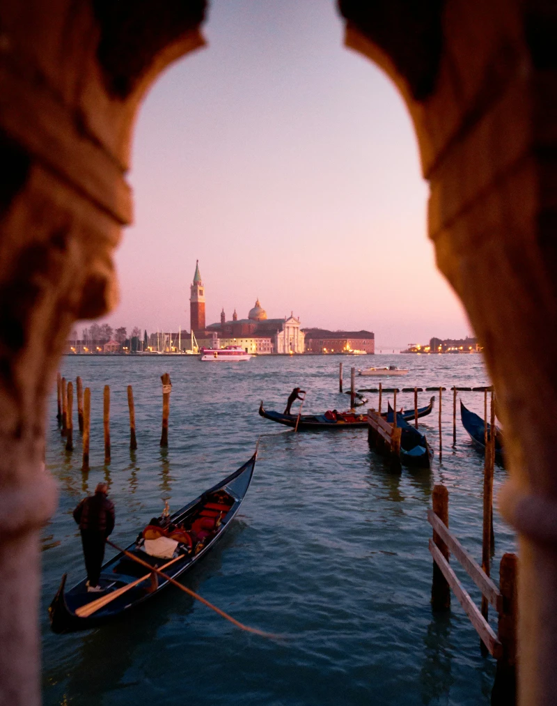 Gondolas on the water at sunset in Venice, Italy, with a view of historical buildings and the iconic bell tower.