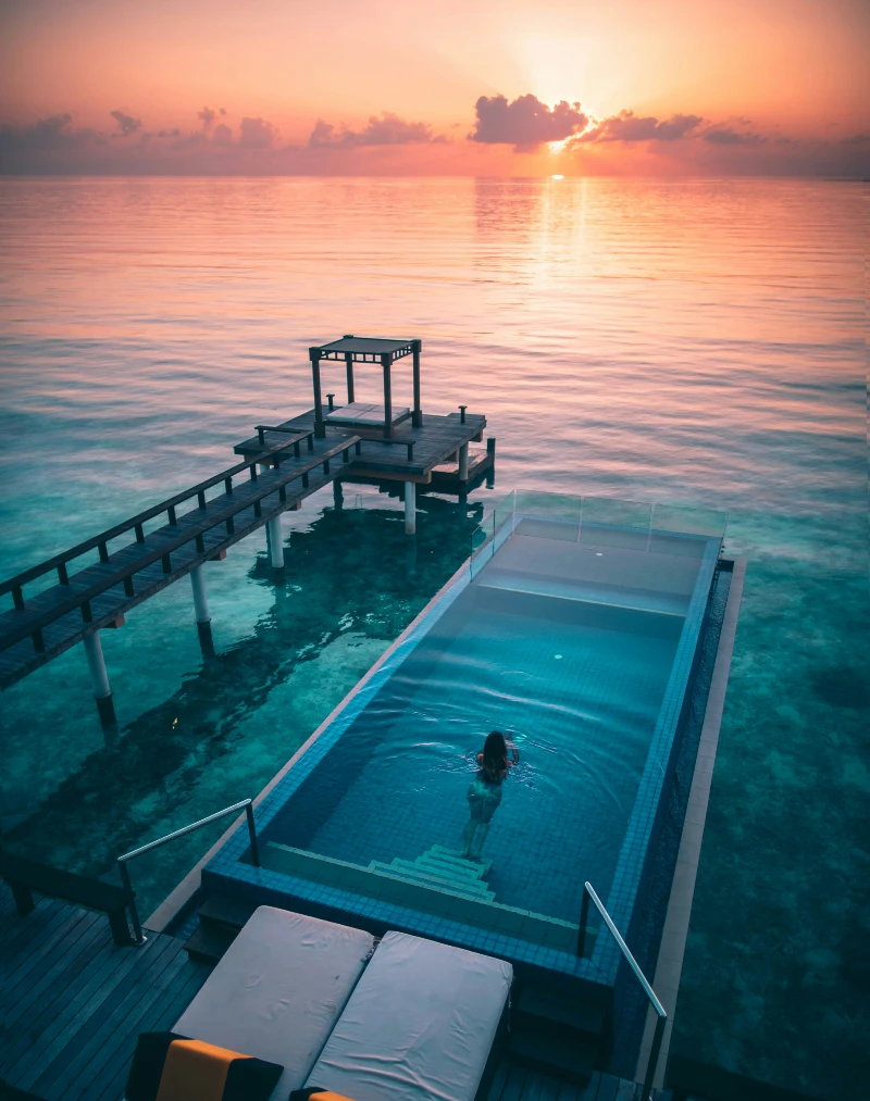 Woman in an infinity pool overlooking a peaceful sunset on the ocean, perfect for a romantic honeymoon getaway in 2025.