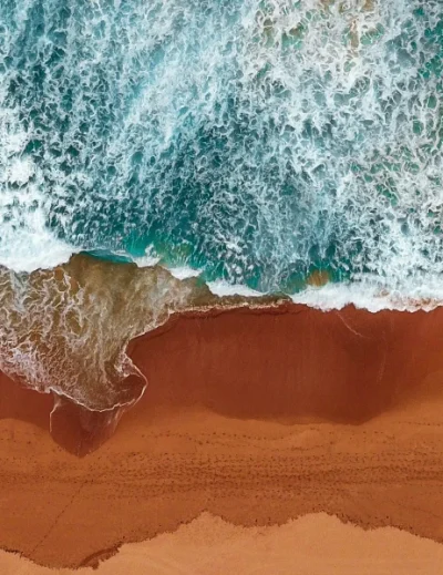 Aerial view of waves crashing onto a sandy beach with two beach chairs, ideal for a relaxing honeymoon getaway in 2025.