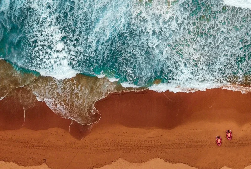 Aerial view of waves crashing onto a sandy beach with two beach chairs, ideal for a relaxing honeymoon getaway in 2025.