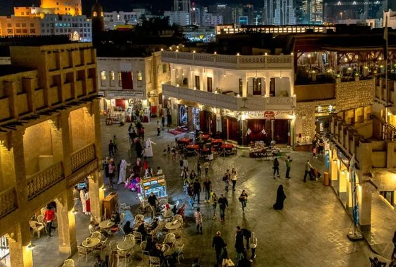 An evening view of Souq Waqif in Qatar, with people shopping, dining, and exploring the lively marketplace under the city lights.