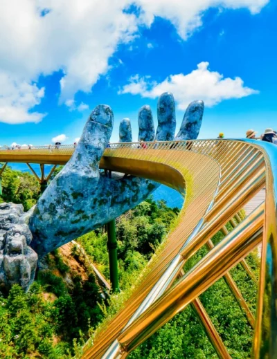 Stunning view of the Golden Bridge at Ba Na Hills, Vietnam, featuring giant stone hands holding the bridge under a clear blue sky.