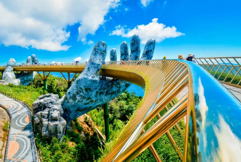 Stunning view of the Golden Bridge at Ba Na Hills, Vietnam, featuring giant stone hands holding the bridge under a clear blue sky.