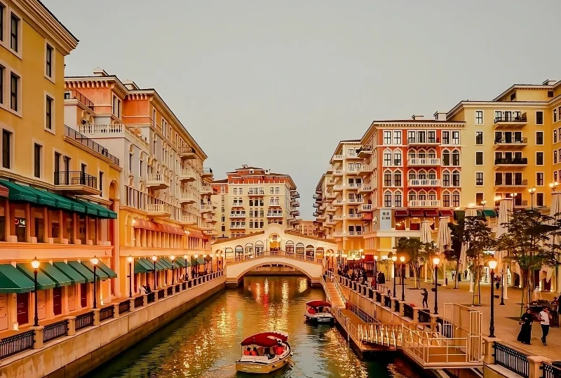 Scenic view of The Pearl Island in Doha, Qatar, featuring a beautiful canal surrounded by luxury apartments and boats under a glowing sunset
