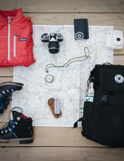 Solo travel essentials including a red jacket, hiking boots, cameras, compass, and backpack for a stress-free journey with Lery Hago Travels.