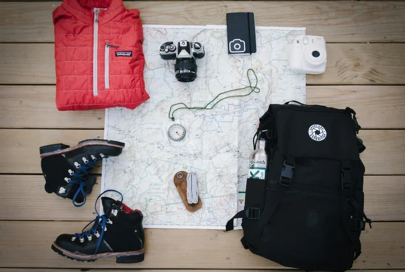 Solo travel essentials including a red jacket, hiking boots, cameras, compass, and backpack for a stress-free journey with Lery Hago Travels.