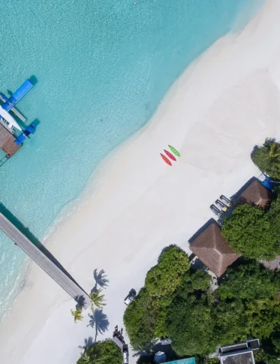 "A stunning aerial view of a Maldives luxury beach resort with crystal-clear waters, kayaks, and a seaplane docked at the pier, ideal for first-timers with Lery Hago Travels."