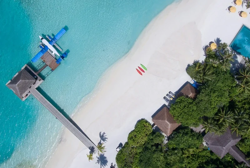 "A stunning aerial view of a Maldives luxury beach resort with crystal-clear waters, kayaks, and a seaplane docked at the pier, ideal for first-timers with Lery Hago Travels."