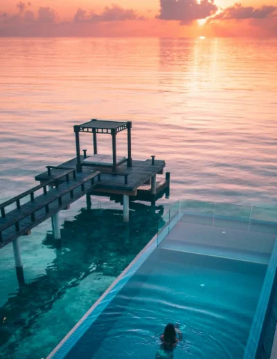 "A serene sunset in the Maldives with a luxury infinity pool overlooking the ocean, perfect for first-time visitors seeking a luxury escape with Lery Hago Travels."