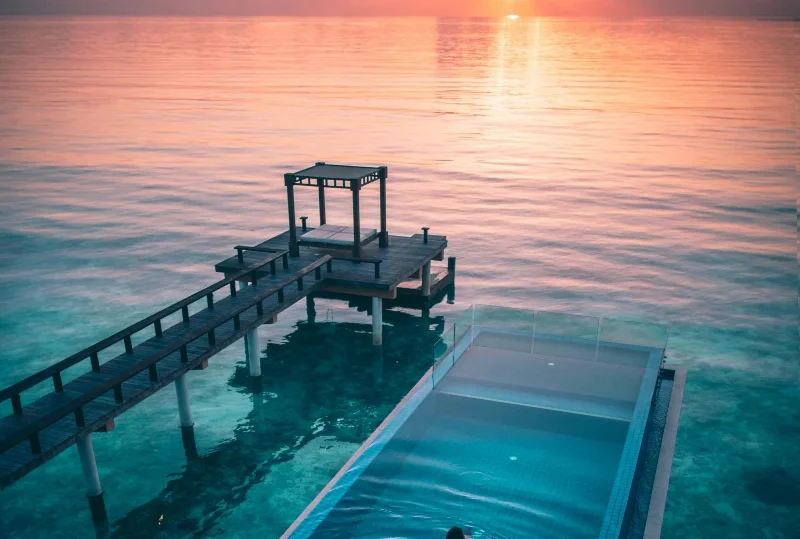 "A serene sunset in the Maldives with a luxury infinity pool overlooking the ocean, perfect for first-time visitors seeking a luxury escape with Lery Hago Travels."