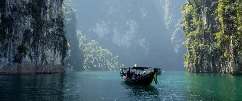 A longtail boat with tourists navigating emerald waters between towering limestone cliffs in Thailand
