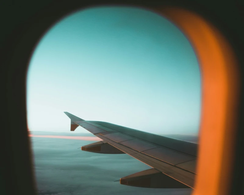 A view of an airplane wing through the window during a flight, highlighting tips on how to survive a long layover by Lery Hago Travels.