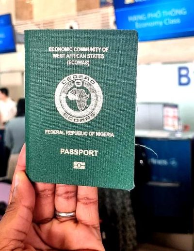 "A person holding a Nigerian passport at an airport check-in counter with airline staff and signage visible in the background."