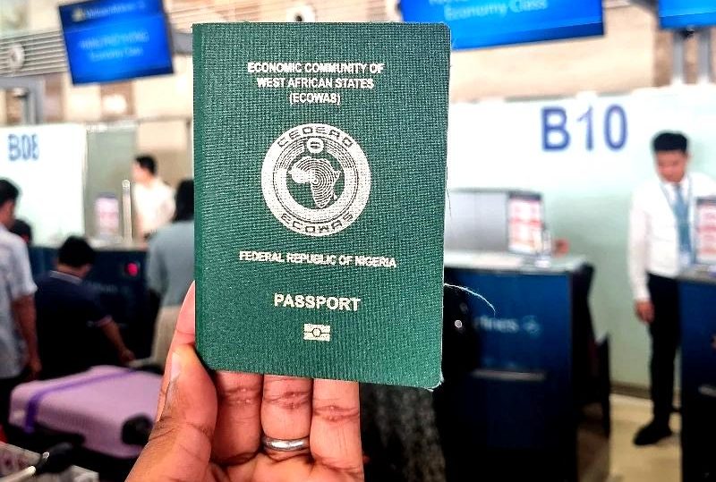 "A person holding a Nigerian passport at an airport check-in counter with airline staff and signage visible in the background."