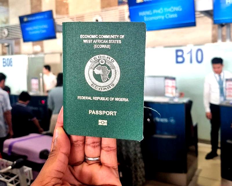 "A person holding a Nigerian passport at an airport check-in counter with airline staff and signage visible in the background."