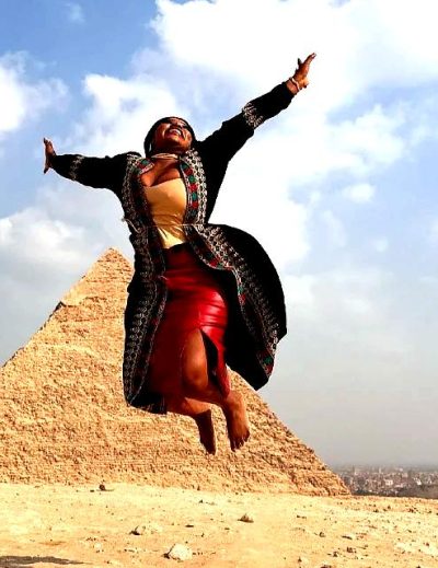 "Smiling woman joyfully jumping in front of the Great Pyramid of Giza, symbolizing adventure and cultural exploration in Egypt."