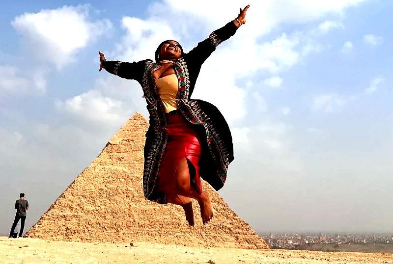 "Smiling woman joyfully jumping in front of the Great Pyramid of Giza, symbolizing adventure and cultural exploration in Egypt."