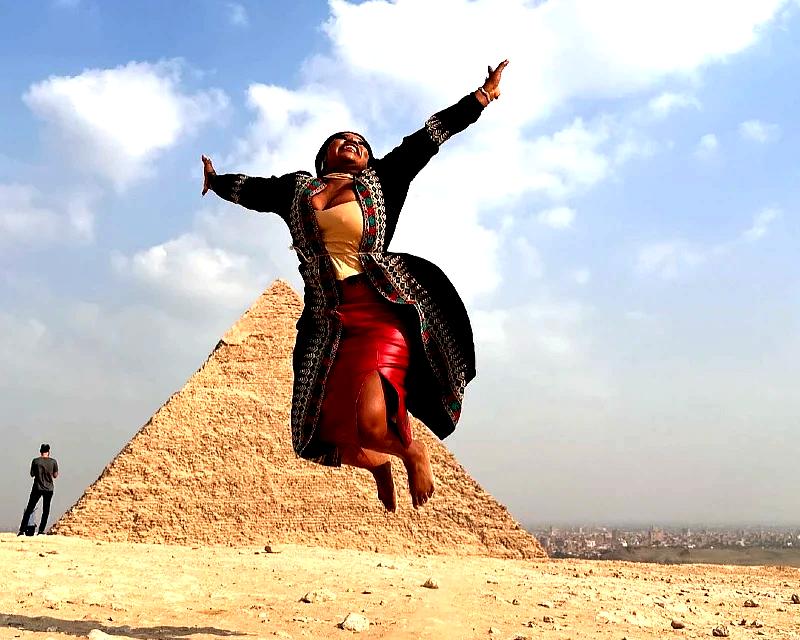 "Smiling woman joyfully jumping in front of the Great Pyramid of Giza, symbolizing adventure and cultural exploration in Egypt."