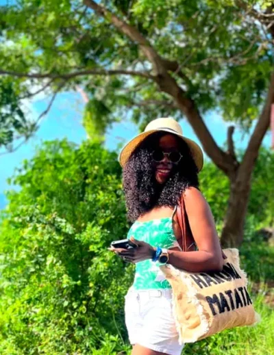 A woman enjoying a sunny day in Zanzibar, standing near lush greenery and overlooking the ocean.