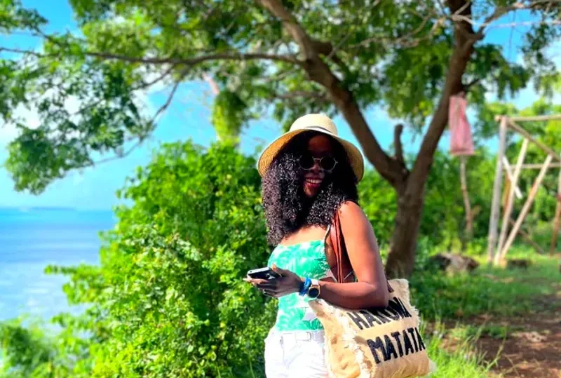 A woman enjoying a sunny day in Zanzibar, standing near lush greenery and overlooking the ocean.