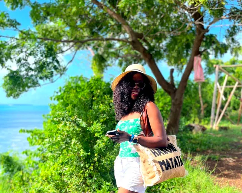 A woman enjoying a sunny day in Zanzibar, standing near lush greenery and overlooking the ocean.