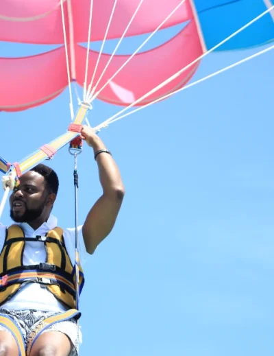 "A man enjoying parasailing under a vibrant parachute against a clear blue sky, showcasing an adventurous holiday experience with Lery Hago Travels."