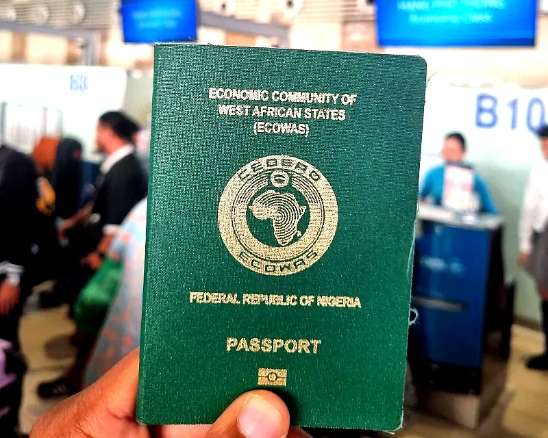 A close-up view of a Nigerian passport held at an airport check-in area, representing travel readiness and documentation.