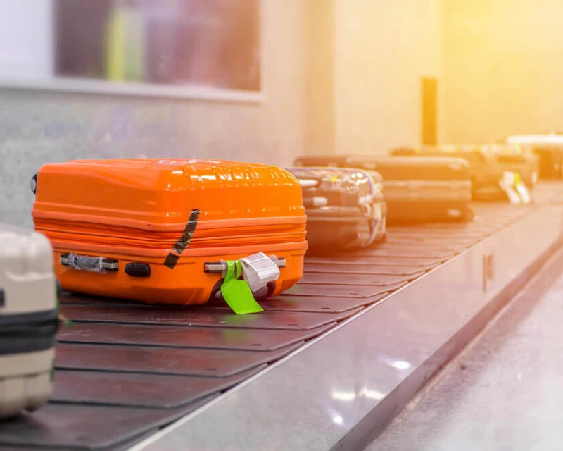 "Bright orange suitcase and other luggage on a conveyor belt at an airport, illustrating prohibited items you shouldn't pack for international travel."