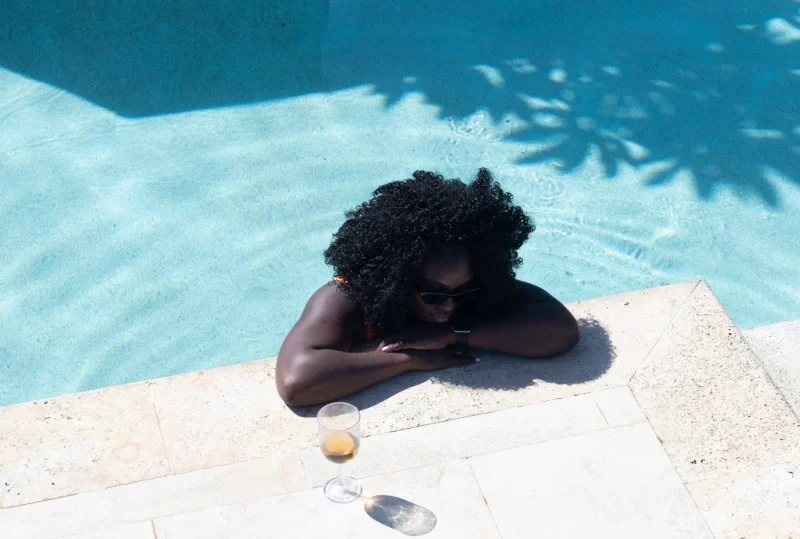 "A woman relaxing at the edge of a pool with a glass of wine nearby, showcasing a luxurious travel experience by Lery Hago Travels."