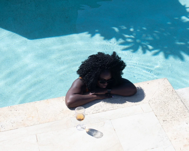 "A woman relaxing at the edge of a pool with a glass of wine nearby, showcasing a luxurious travel experience by Lery Hago Travels."