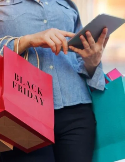 "A woman holding a tablet with shopping bags labeled 'Black Friday,' showcasing essential travel deals and discounts from Lery Hago Travels."