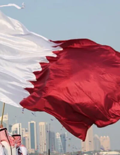 Qatar national flag waving against the backdrop of a city skyline during Qatar National Day 2024.