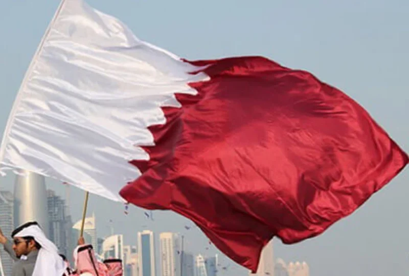 Qatar national flag waving against the backdrop of a city skyline during Qatar National Day 2024.