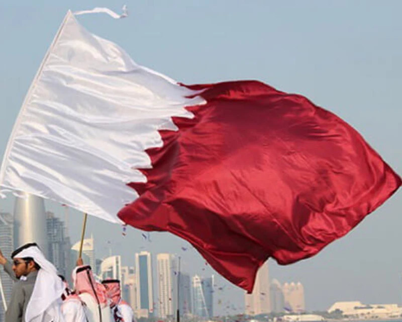 Qatar national flag waving against the backdrop of a city skyline during Qatar National Day 2024.