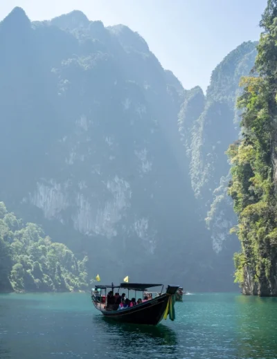 "A traditional boat gliding through turquoise waters surrounded by towering limestone cliffs on a sunny day, showcasing a serene travel destination.