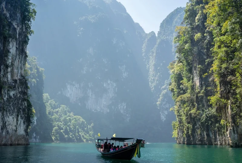 "A traditional boat gliding through turquoise waters surrounded by towering limestone cliffs on a sunny day, showcasing a serene travel destination.