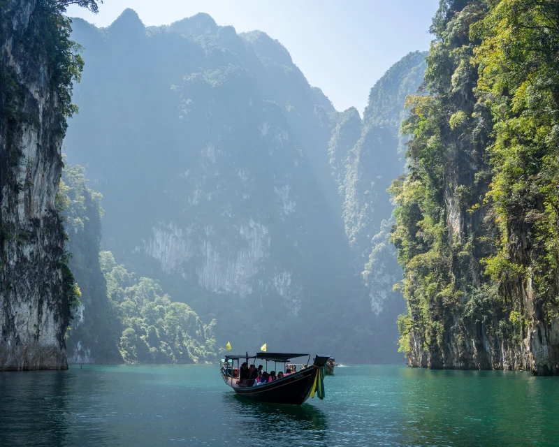 "A traditional boat gliding through turquoise waters surrounded by towering limestone cliffs on a sunny day, showcasing a serene travel destination.