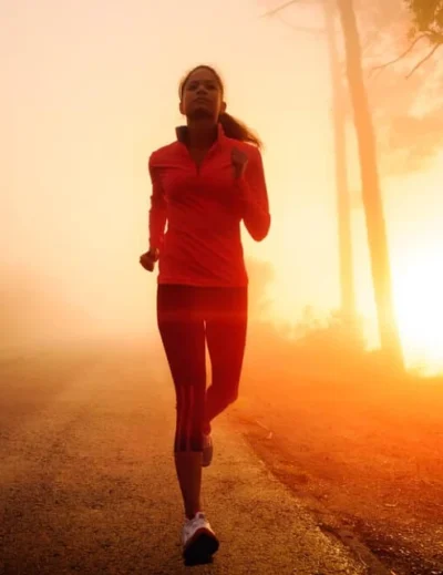 "A woman jogging along a foggy road at sunrise, symbolizing fitness and motivation for marathon preparation in 2025."