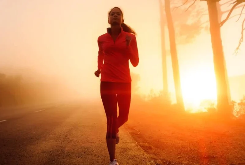 "A woman jogging along a foggy road at sunrise, symbolizing fitness and motivation for marathon preparation in 2025."