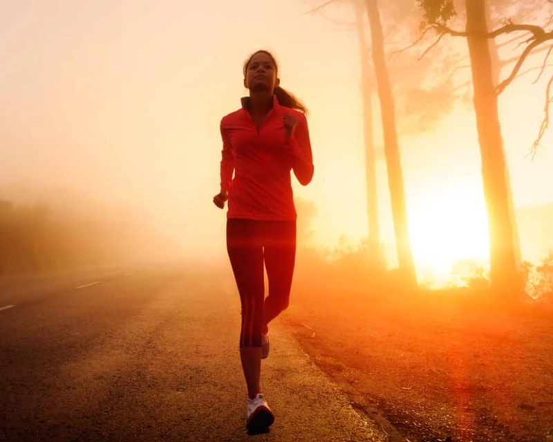 "A woman jogging along a foggy road at sunrise, symbolizing fitness and motivation for marathon preparation in 2025."