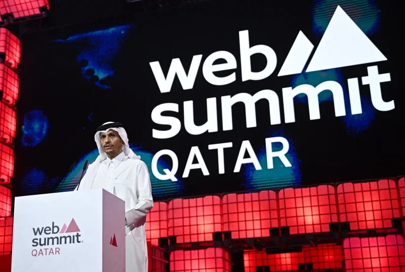 A speaker dressed in traditional Qatari attire delivering a keynote address at Qatar Web Summit 2025, with the event logo displayed prominently in the background.