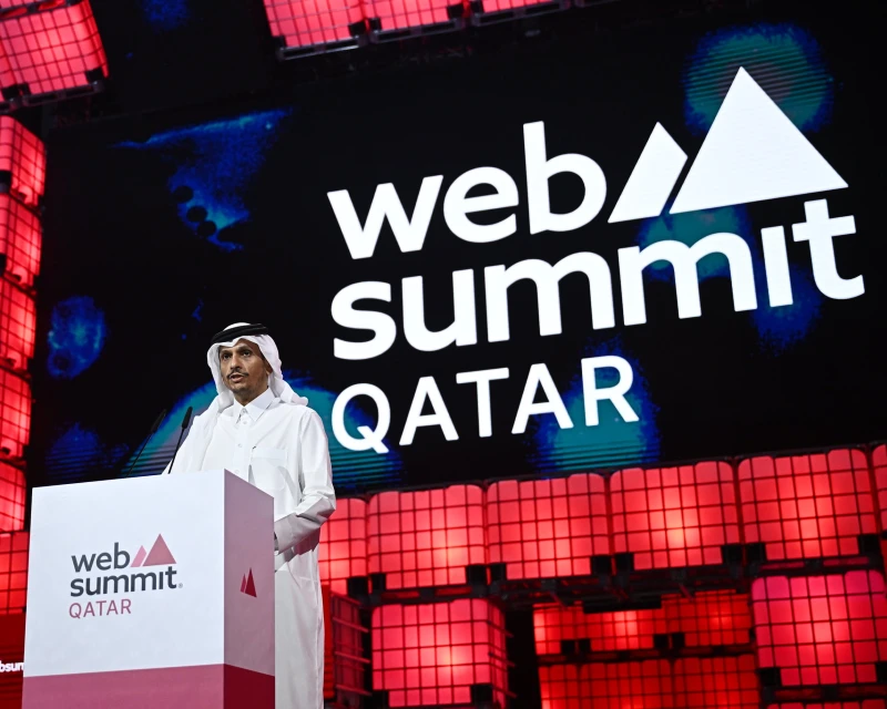 A speaker dressed in traditional Qatari attire delivering a keynote address at Qatar Web Summit 2025, with the event logo displayed prominently in the background.