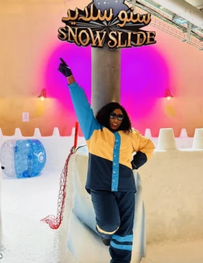 "A stylish traveler poses in front of the Snow Slide attraction in Qatar, showcasing a vibrant indoor snow experience."