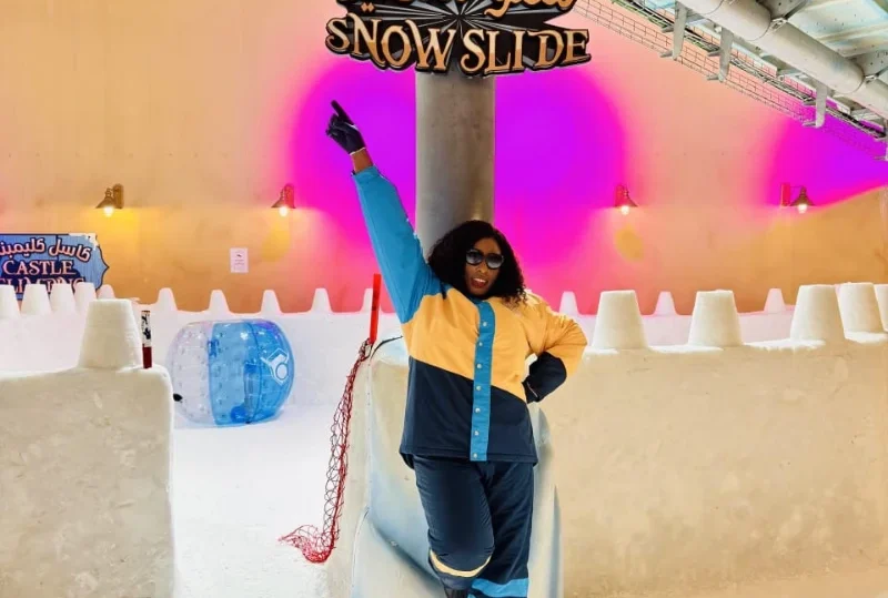 "A stylish traveler poses in front of the Snow Slide attraction in Qatar, showcasing a vibrant indoor snow experience."