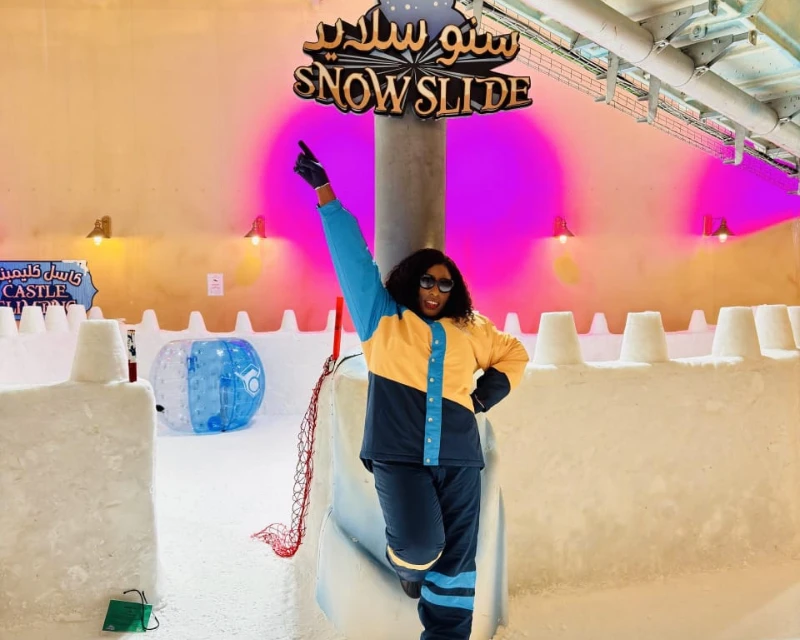 "A stylish traveler poses in front of the Snow Slide attraction in Qatar, showcasing a vibrant indoor snow experience."