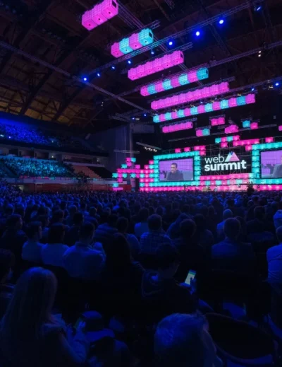 "Web Summit Qatar 2025 event showcasing a large audience and an illuminated main stage with speakers."